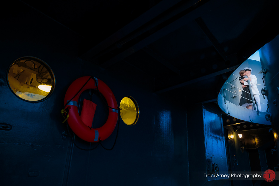 view from inside battleship of couple kissing on deck during engagement session in Wilmington, NC